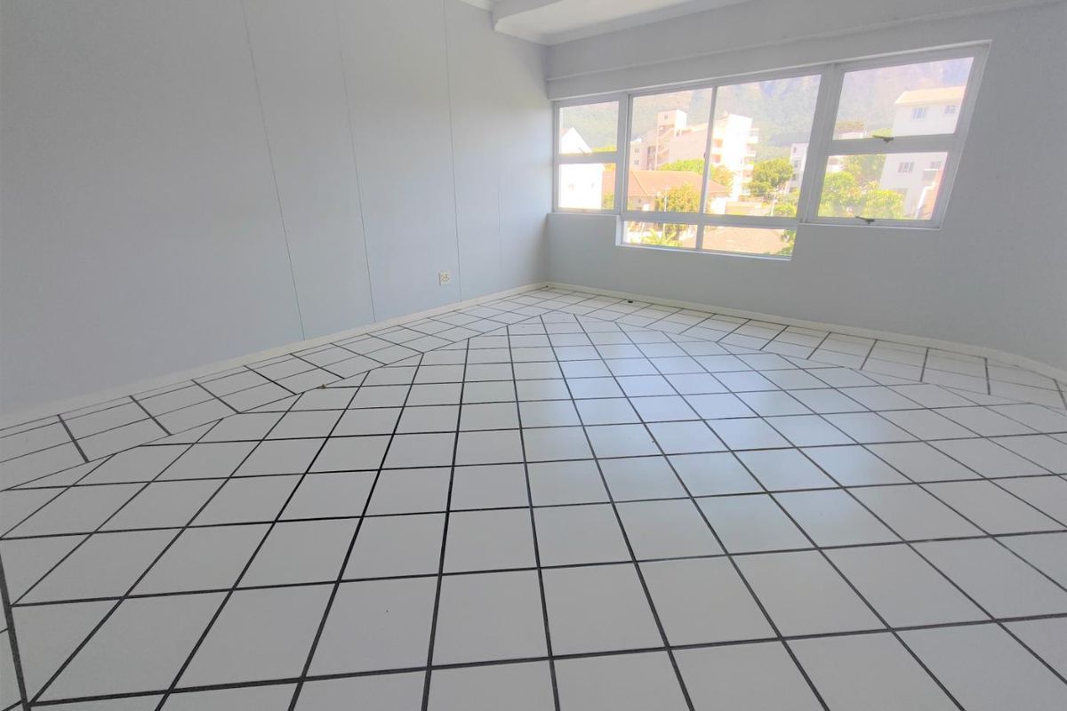 A bright, empty living area featuring large windows and distinctive diamond-patterned floor tiles, offering a blank canvas for interior design.