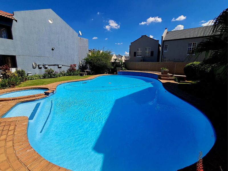 A well-maintained swimming pool area featuring brick coping, surrounding landscaped garden, and secure boundary walls within a townhouse complex.