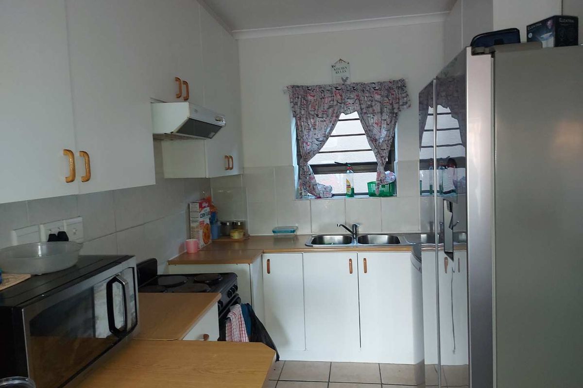 A functional kitchen featuring white cabinetry, a double basin sink, tiled splashbacks, and tiled flooring, offering a practical layout for daily meal preparation.