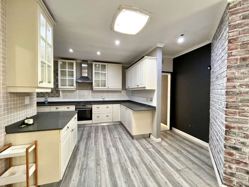 A functional kitchen featuring built-in cabinetry, an integrated oven with extractor fan, laminate flooring, and a distinctive exposed brick feature wall.