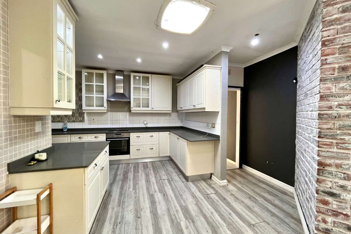 A functional kitchen featuring built-in cabinetry, an integrated oven with extractor fan, laminate flooring, and a distinctive exposed brick feature wall.