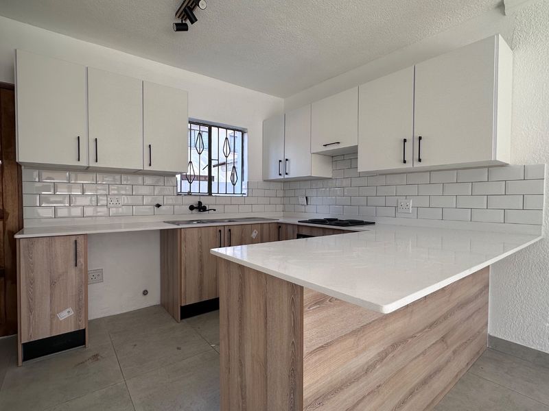 A modern, newly renovated kitchen featuring white subway tile backsplashes, quartz countertops, and contemporary wood-finish cabinetry with a functional layout.