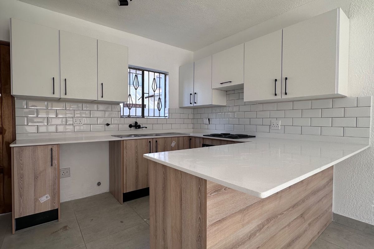 A modern, newly renovated kitchen featuring white subway tile backsplashes, quartz countertops, and contemporary wood-finish cabinetry with a functional layout.