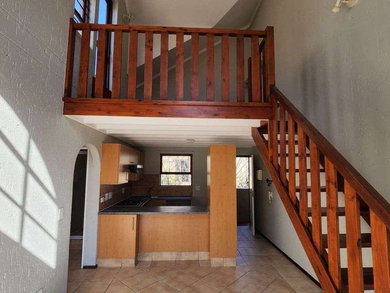 Open-plan living area featuring a wooden staircase leading to a mezzanine level, with an integrated kitchen and tiled flooring throughout.