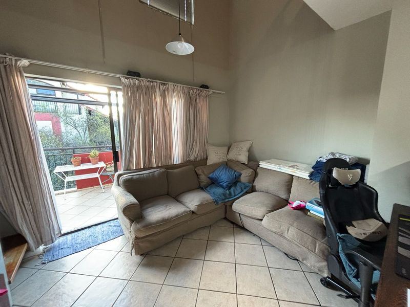 A living room featuring tiled flooring, a vaulted ceiling, and a sliding glass door providing access to an outdoor balcony.