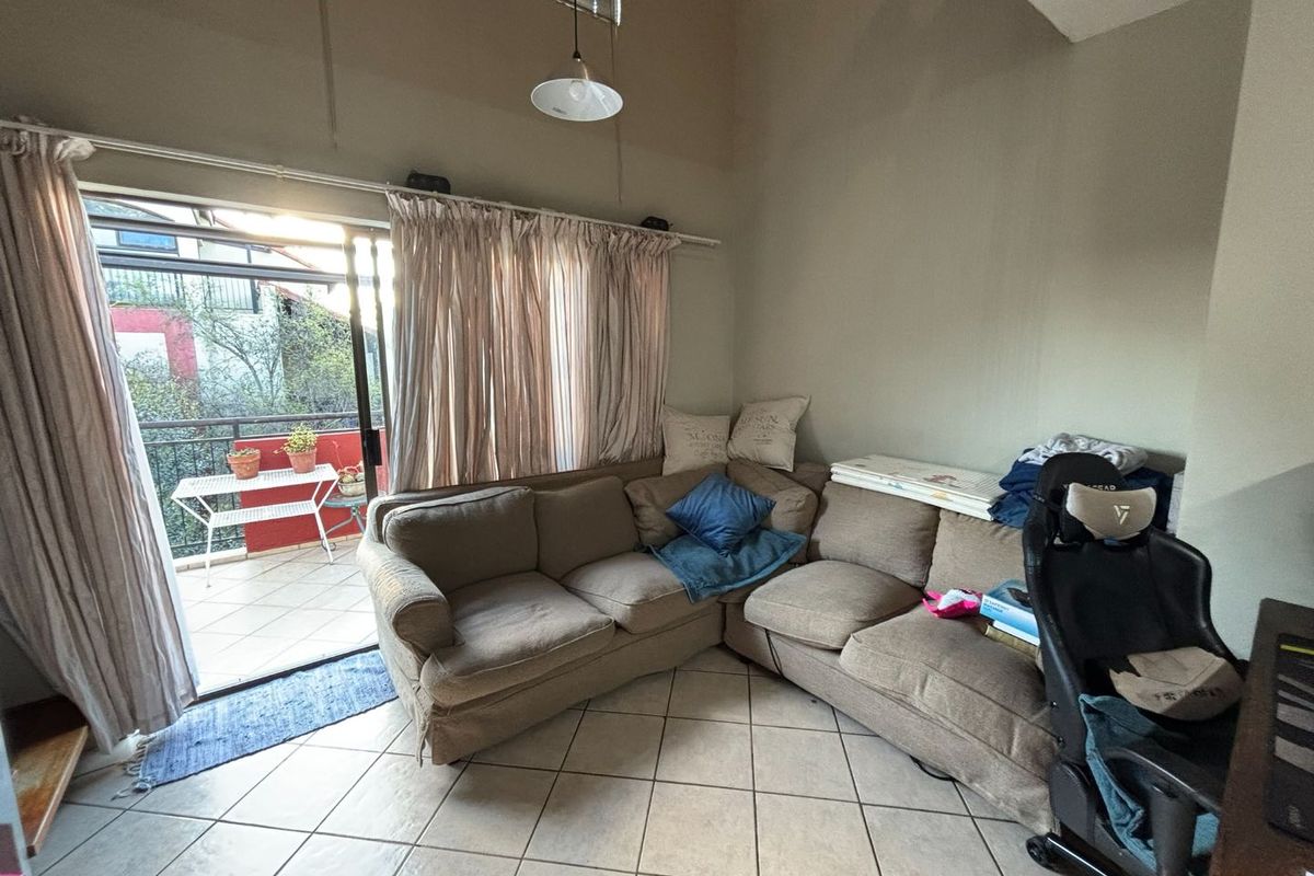 A living room featuring tiled flooring, a vaulted ceiling, and a sliding glass door providing access to an outdoor balcony.