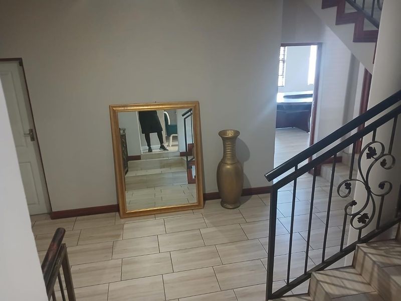 A bright hallway featuring tiled flooring and a decorative wrought iron staircase railing, leading towards an adjacent office space.