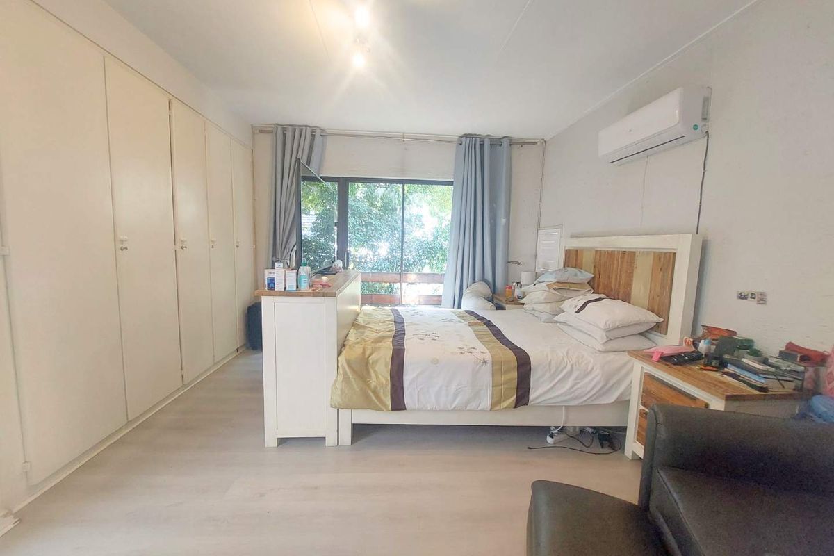 Spacious bedroom featuring extensive built-in cabinetry, light-toned flooring, and a wall-mounted air conditioning unit with access to an outdoor balcony.