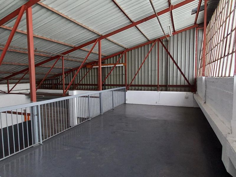 An open-plan industrial mezzanine level featuring exposed steel trusses, metal roofing, and large steel-framed windows, providing a versatile elevated workspace.