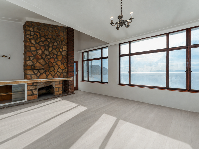 Spacious living room featuring a prominent stone fireplace, built-in cabinetry, and expansive windows offering scenic coastal views with abundant natural light.
