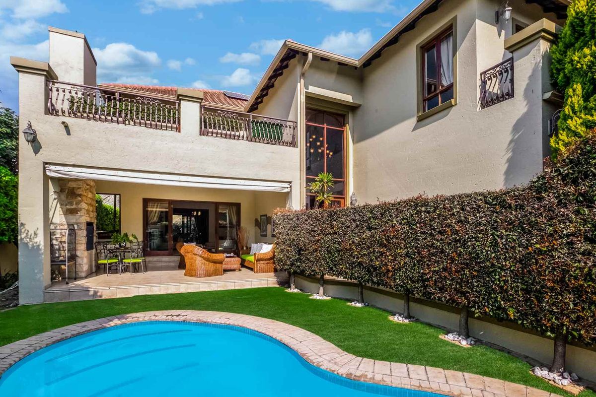 Rear exterior view featuring a swimming pool, tiled patio with built-in braai, and an upper-level balcony with wrought iron railings.