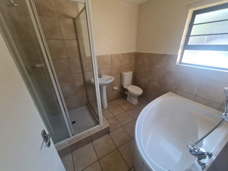 A functional bathroom featuring a corner bathtub, separate shower enclosure, pedestal basin, and toilet with neutral tiled finishes.