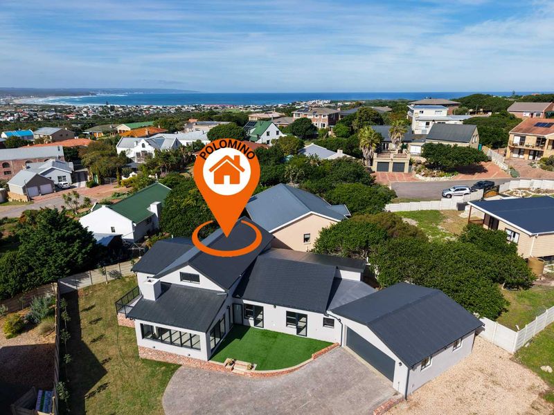 Aerial view of the property showcasing the roof structure, driveway, garage, and landscaped garden area with a coastal backdrop.
