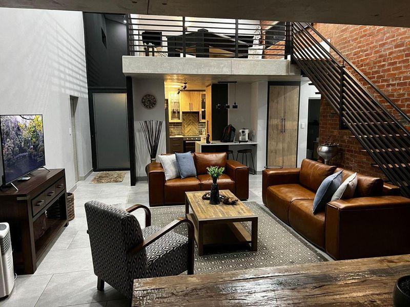 Modern open-plan living area featuring a mezzanine level, exposed brickwork, industrial-style staircase, and a contemporary kitchen with integrated cabinetry.