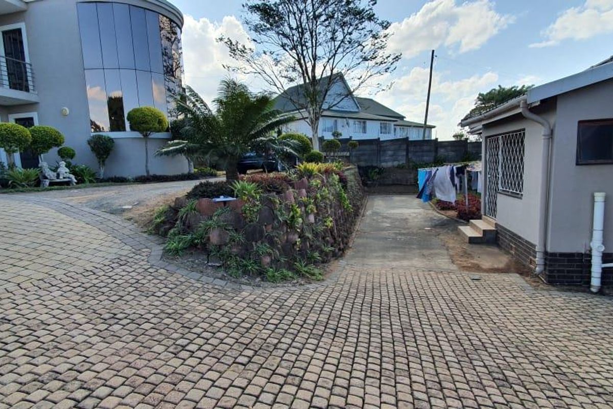 A view of the rear exterior area featuring a paved driveway, a landscaped retaining wall, and access to the side of the property.