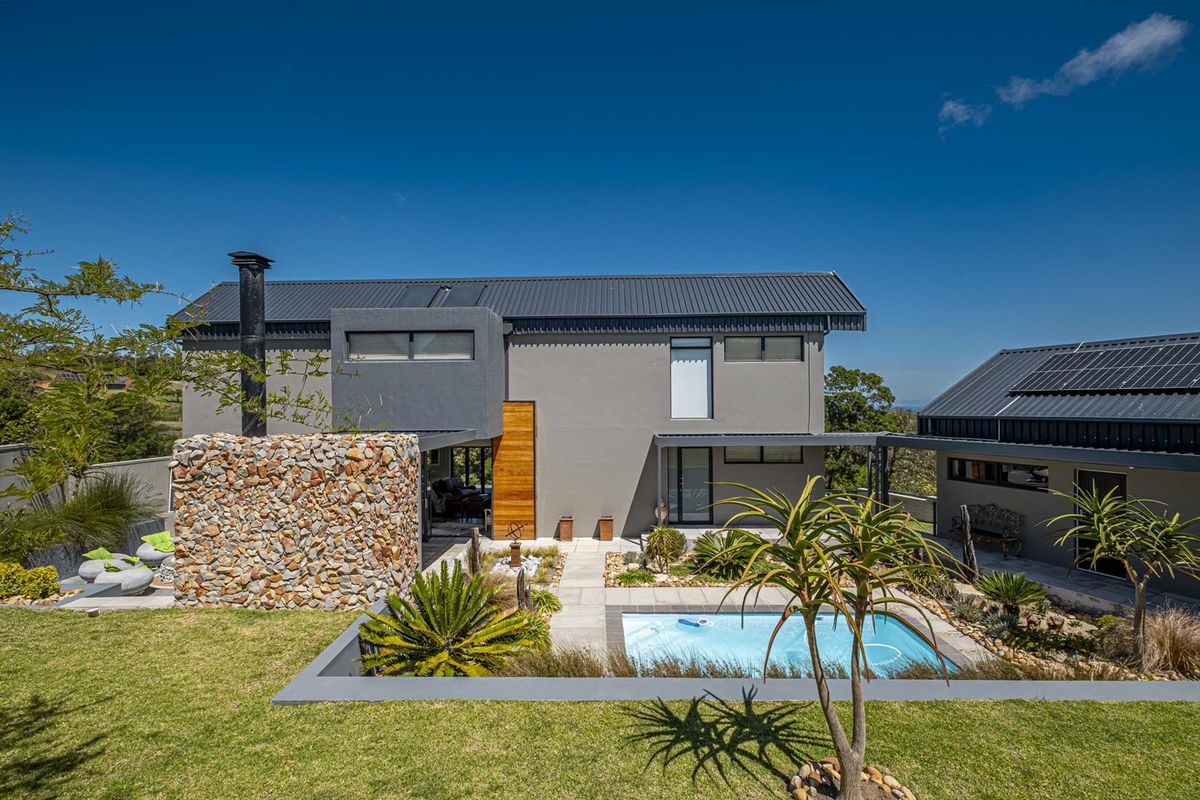Modern two-story residence featuring a stone-clad fireplace, swimming pool, landscaped garden, and solar panels on a contemporary metal roof.