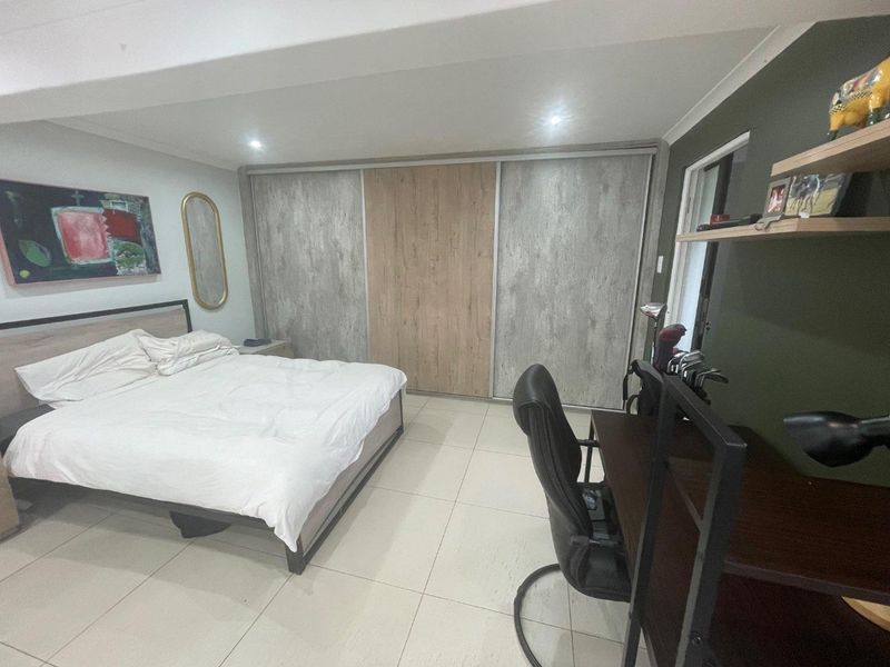 A well-maintained bedroom featuring large built-in sliding door wardrobes, neutral tiled flooring, and recessed ceiling lighting.