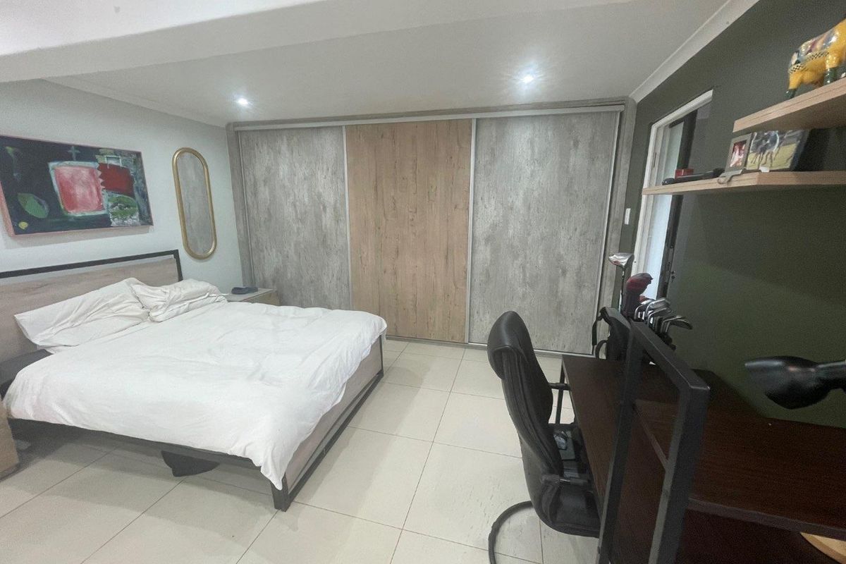 A well-maintained bedroom featuring large built-in sliding door wardrobes, neutral tiled flooring, and recessed ceiling lighting.