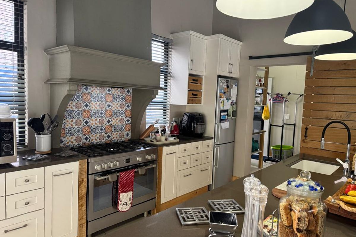 A well-appointed kitchen featuring a large gas range with a decorative tiled backsplash, custom cabinetry, and a central island with a stone countertop.