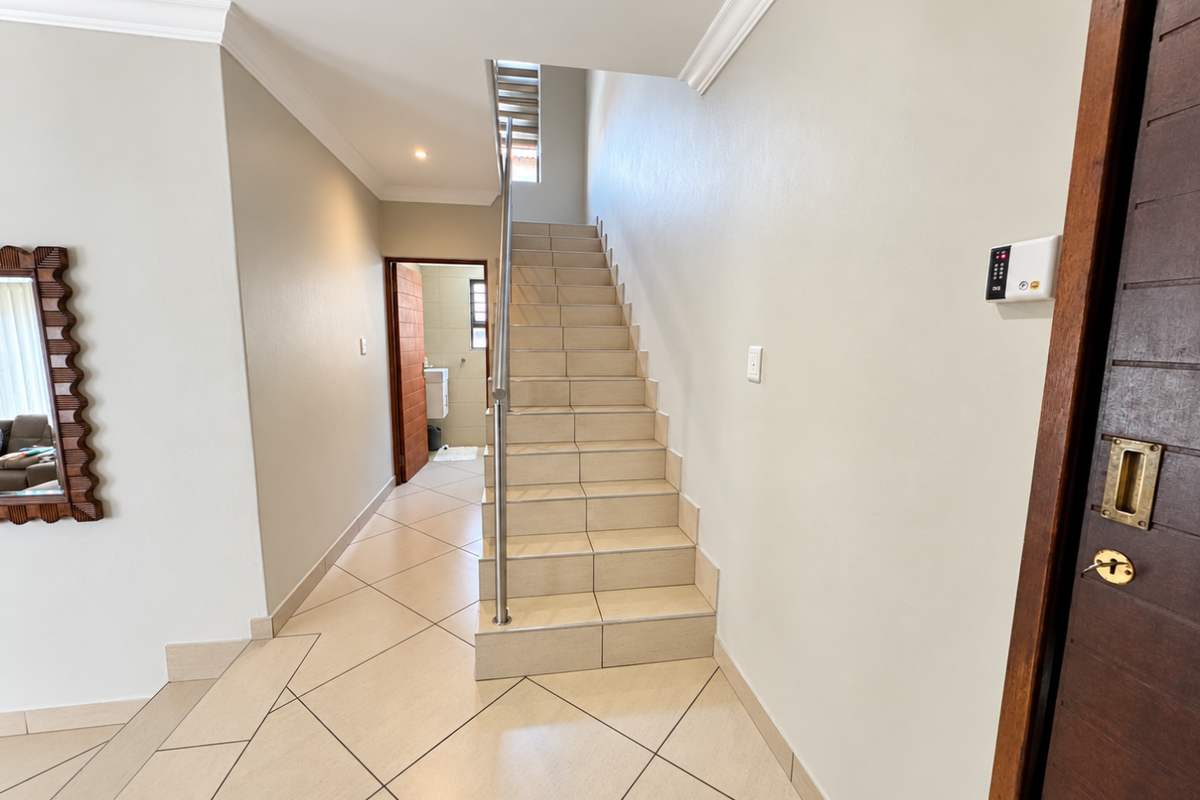 A bright, tiled hallway featuring a staircase with a stainless steel handrail, crown molding, and a secure entrance door.