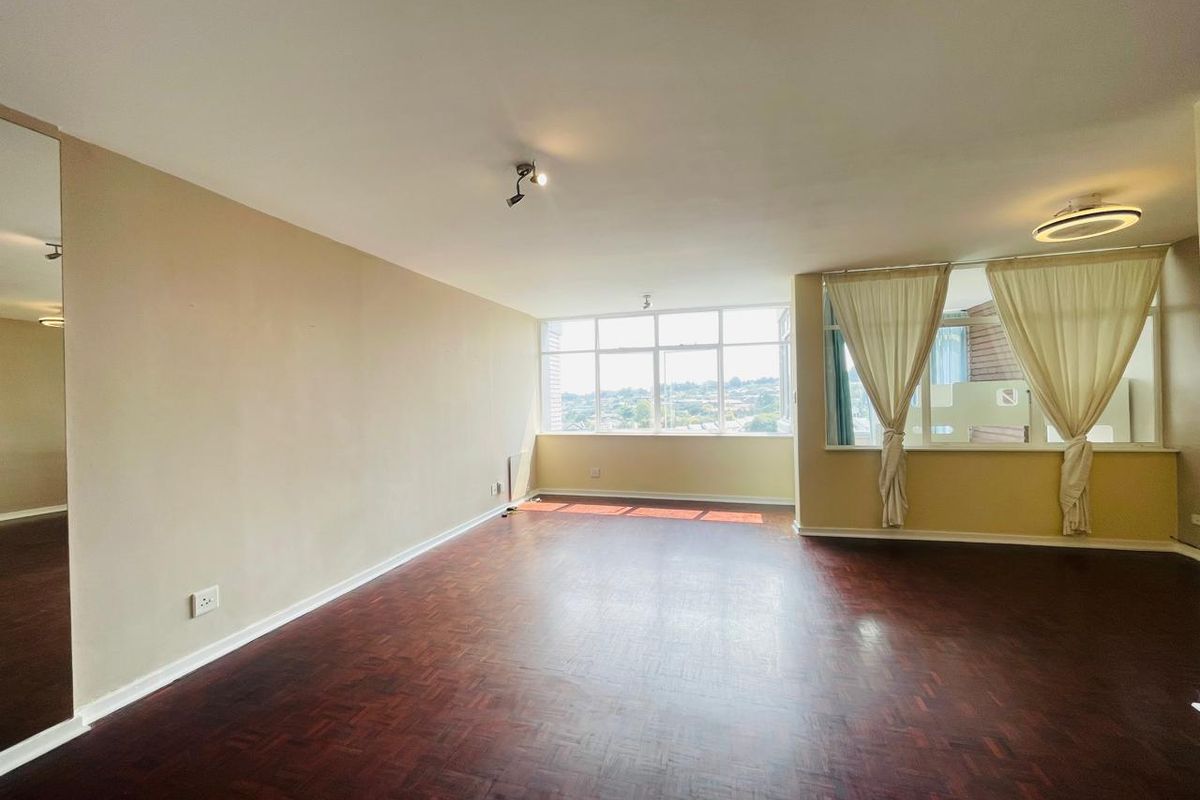 Spacious living area featuring dark parquet flooring, large windows providing natural light, and neutral wall finishes.