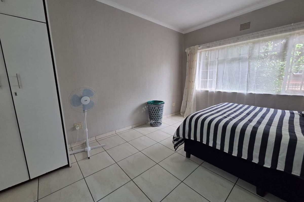 A bedroom featuring tiled flooring, built-in cupboards, and a large window allowing natural light.