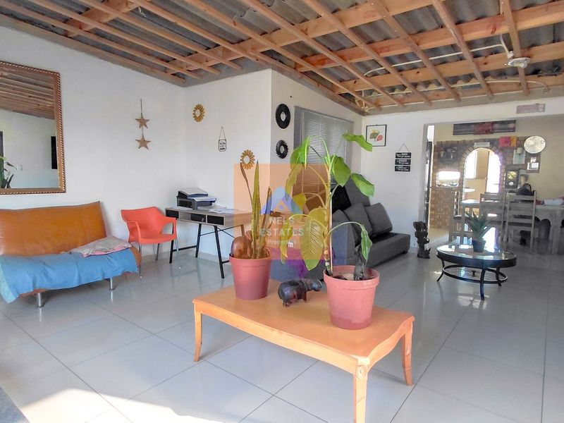 Open-plan living area featuring tiled flooring and an exposed timber ceiling structure, leading through an archway to the dining space.