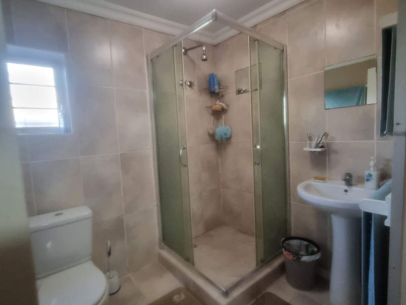A functional bathroom featuring a corner shower enclosure, pedestal basin, and toilet with neutral wall and floor tiling.