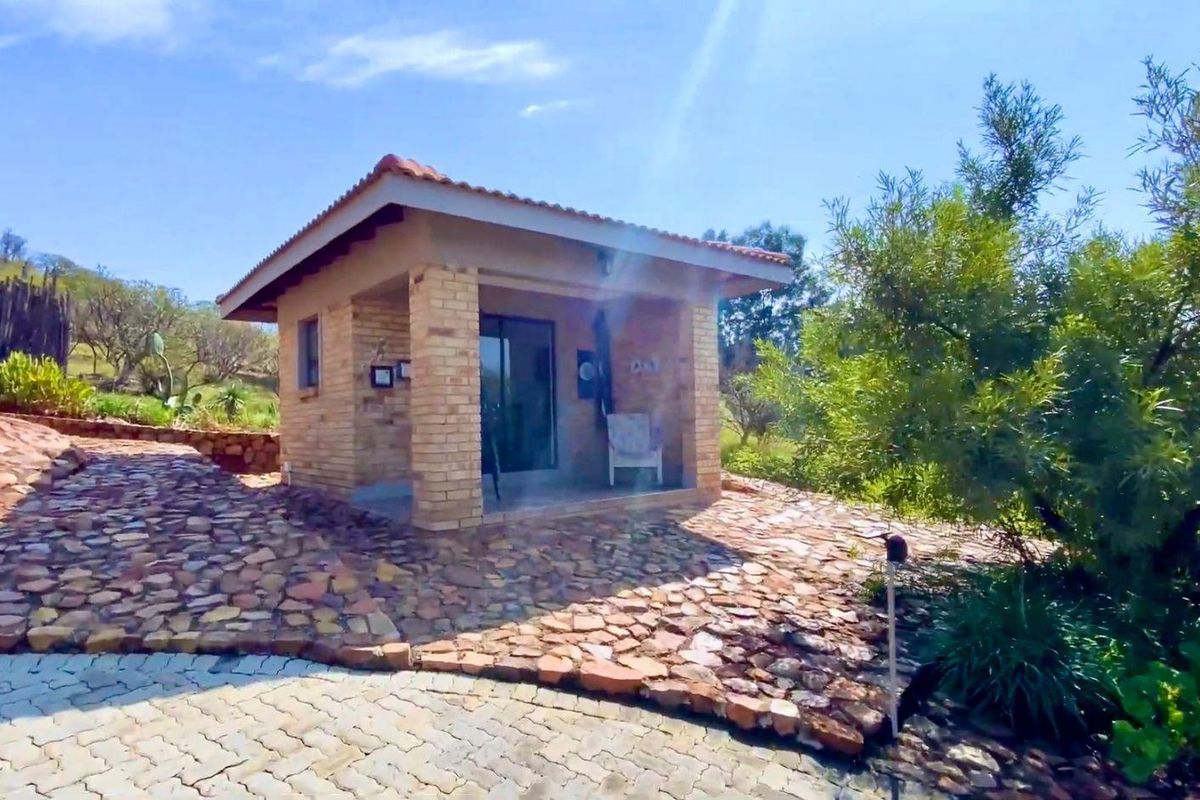 A detached brick structure with a tiled roof and covered patio area, set within a landscaped garden with stone paving.