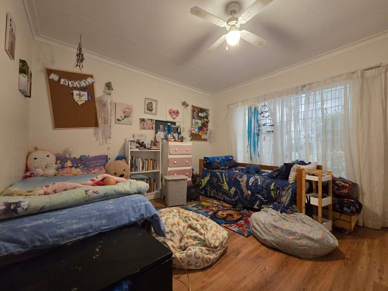 A functional bedroom featuring laminate flooring, a ceiling fan, and large windows with curtain tracks, offering a comfortable living space.