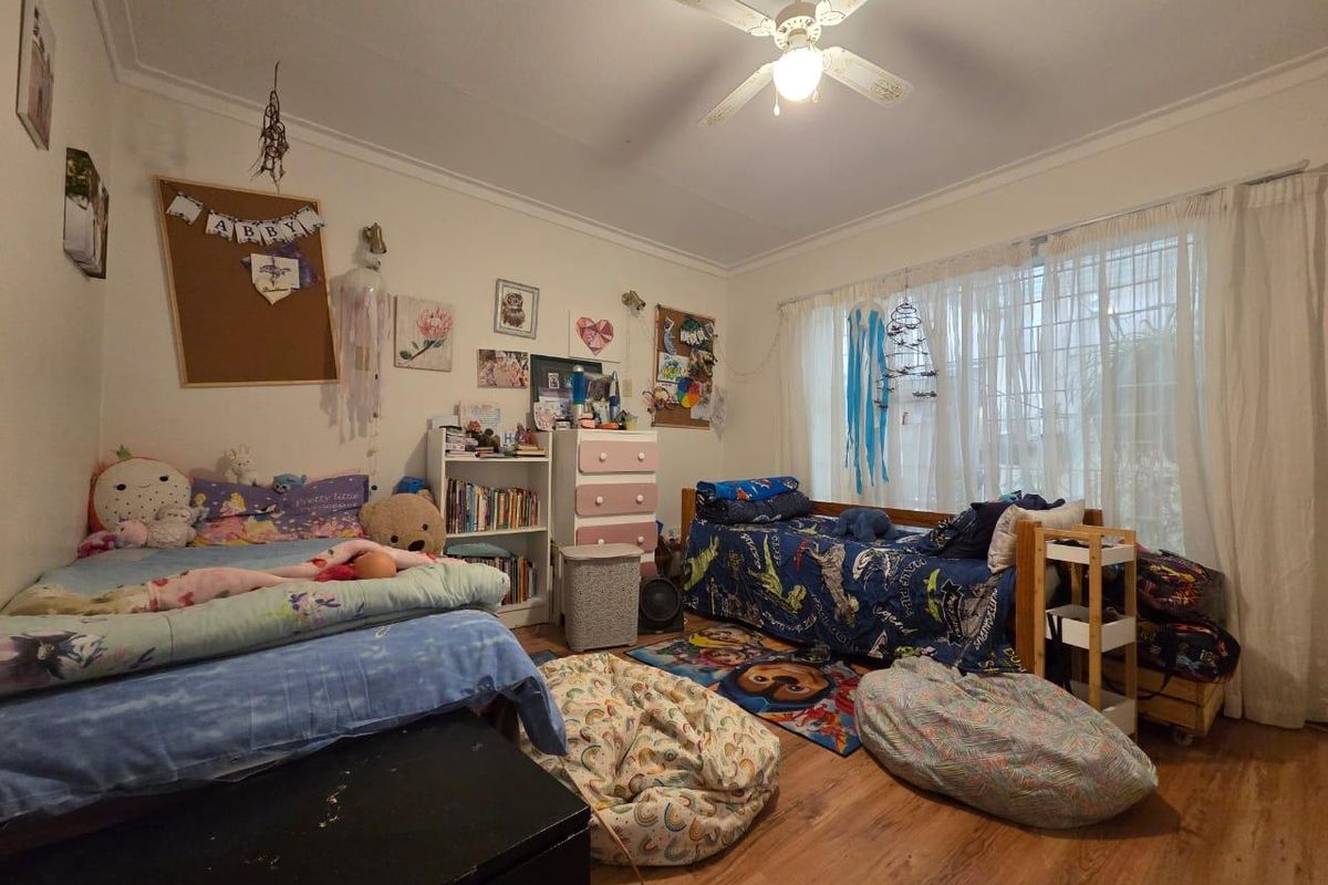 A functional bedroom featuring laminate flooring, a ceiling fan, and large windows with curtain tracks, offering a comfortable living space.