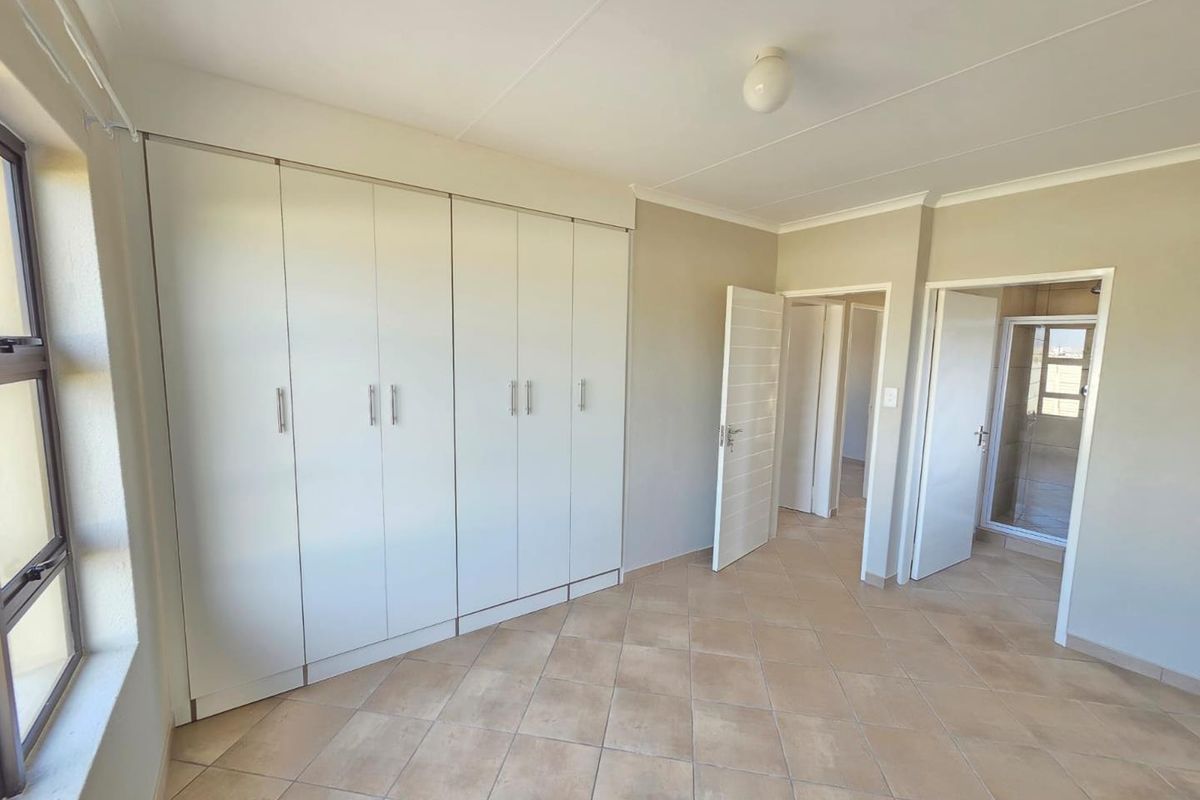A bright bedroom featuring built-in cupboards, tiled flooring, and an en-suite bathroom entrance.