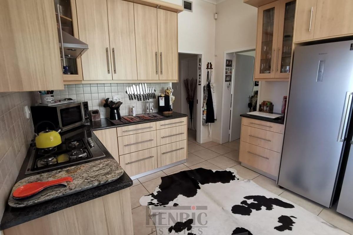 A functional kitchen featuring light wood cabinetry, granite countertops, a gas hob with extractor, and tiled flooring throughout.