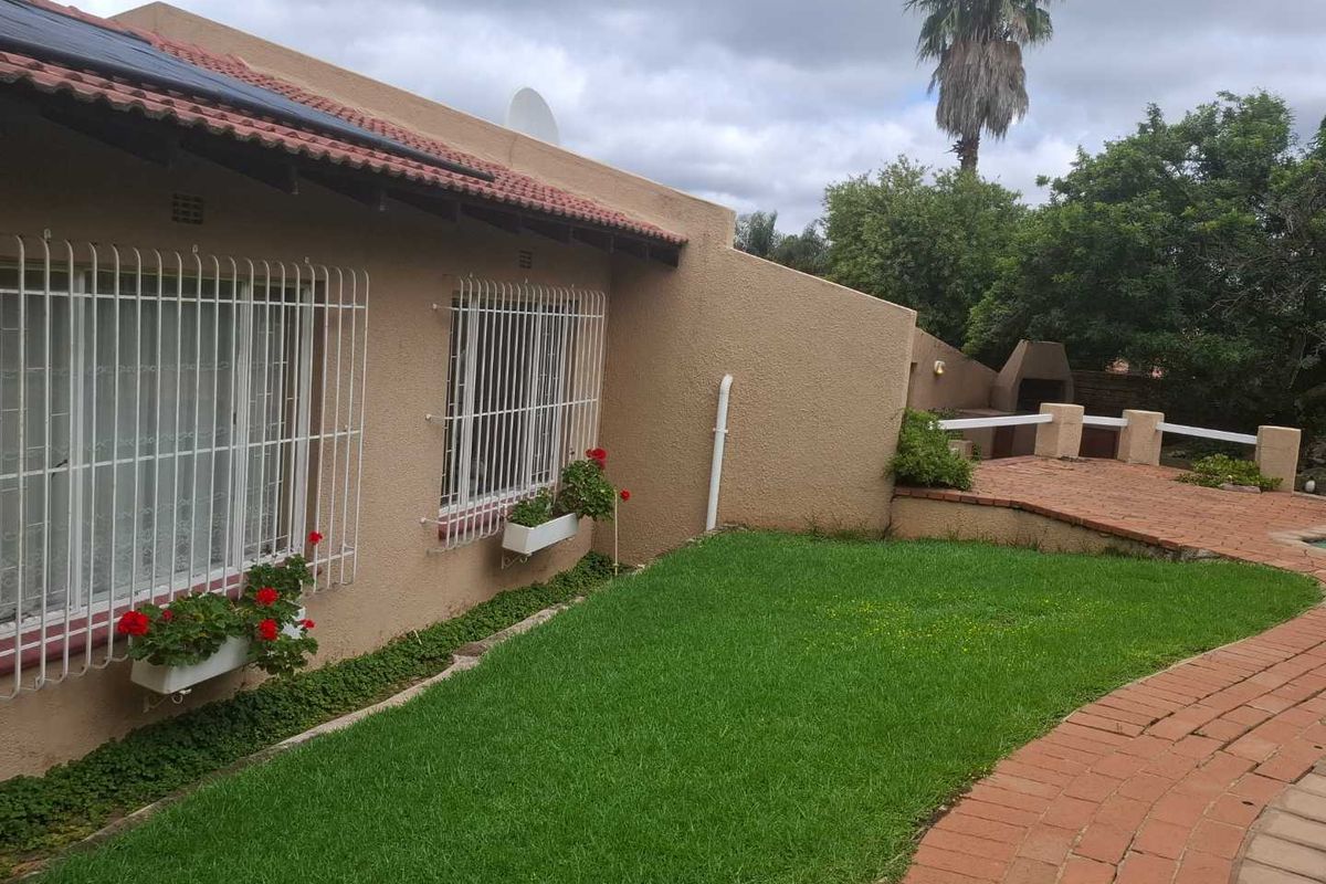 Rear exterior view featuring a lawn, brick paved pathway, and a built-in outdoor braai area against the house wall.