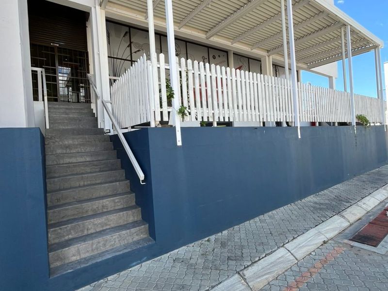 Front exterior view of the office building featuring a raised covered patio, white picket fencing, and concrete staircase access.