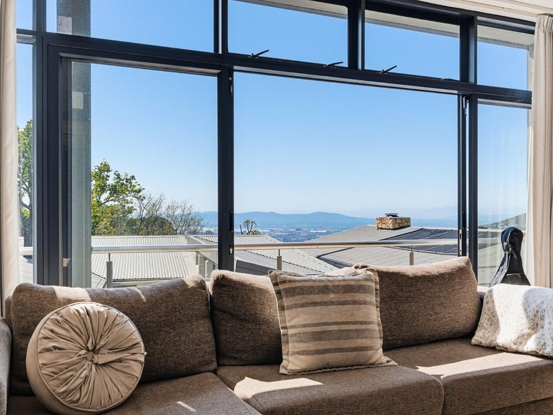 A bright living room featuring expansive floor-to-ceiling windows that offer panoramic views of the surrounding landscape and distant mountains.