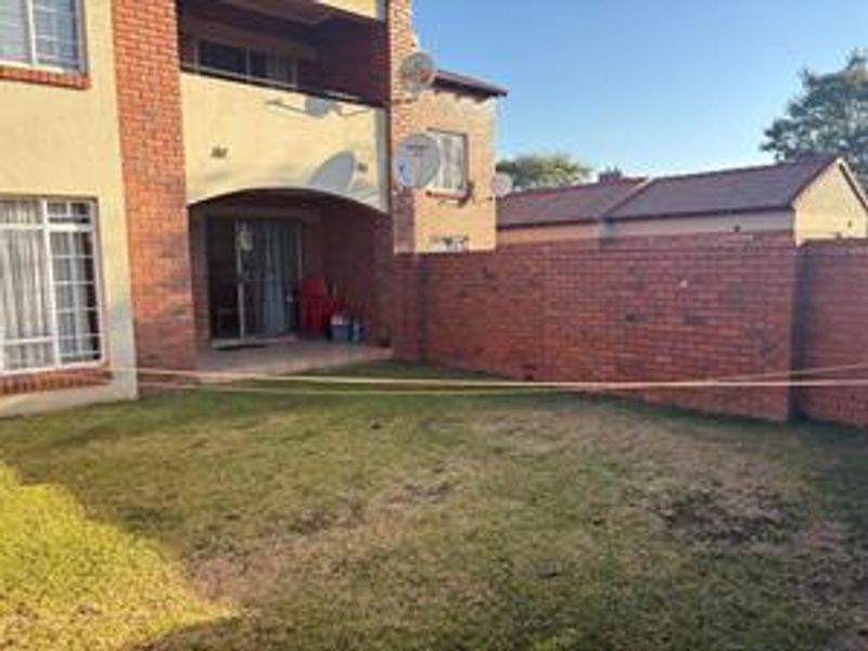 Rear view of the apartment featuring a private garden, brick boundary wall, and a covered patio area with sliding door access.