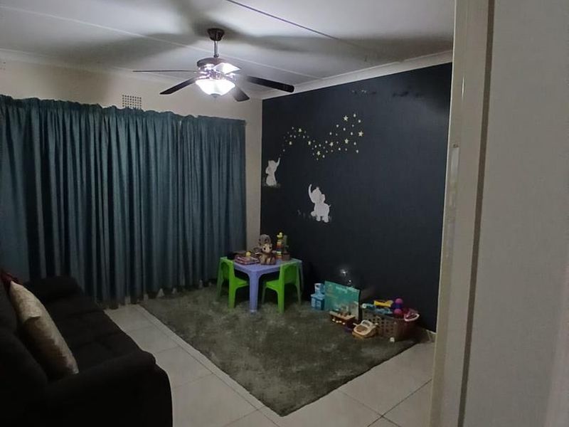 A living room featuring tiled flooring, a ceiling fan, and a dark accent wall, currently utilized as a play area.