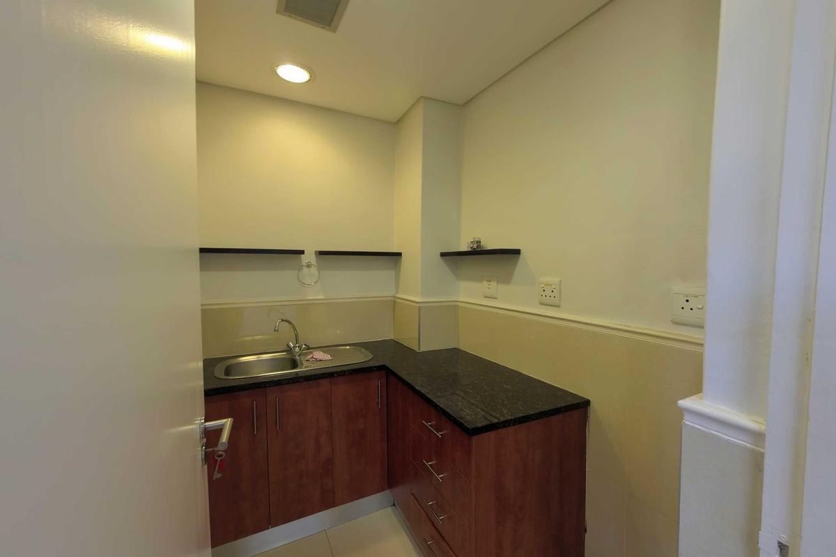 A compact kitchenette area featuring dark granite countertops, wooden cabinetry, a stainless steel sink, and wall-mounted shelving.