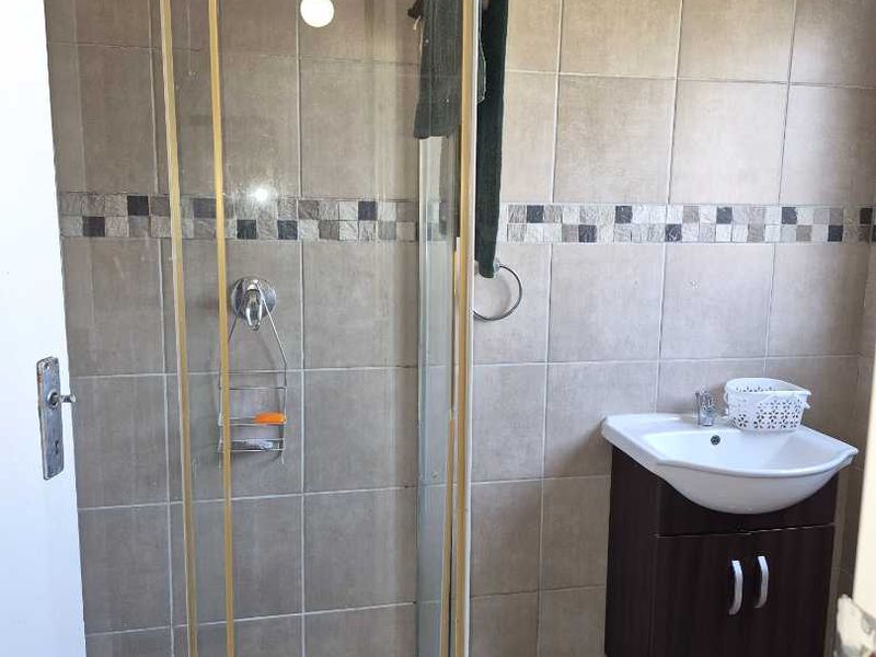 A functional bathroom featuring a shower enclosure with mosaic floor tiling, a vanity basin with storage cabinet, and neutral wall tiles.