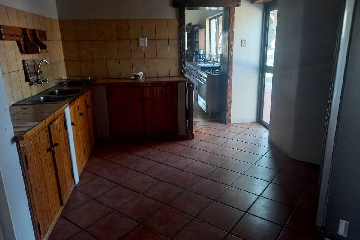 A functional kitchen area featuring wooden cabinetry, tiled splashbacks, and terracotta floor tiles, with an adjacent scullery visible through the doorway.
