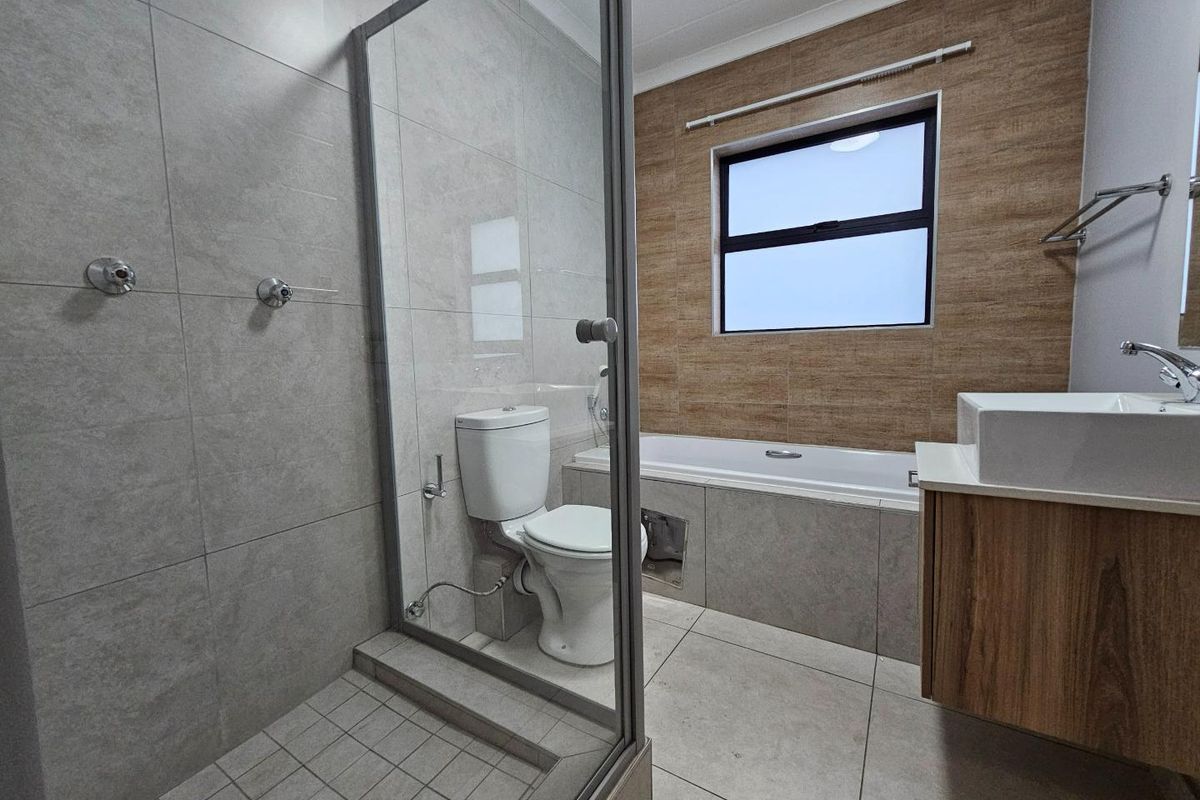 Modern bathroom featuring a glass-enclosed shower, a built-in bathtub, a vanity with a basin, and contemporary neutral wall and floor tiling.