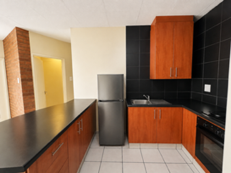 A functional kitchen featuring wood-finish cabinetry, black countertops, a built-in oven, and a contrasting black tiled backsplash.