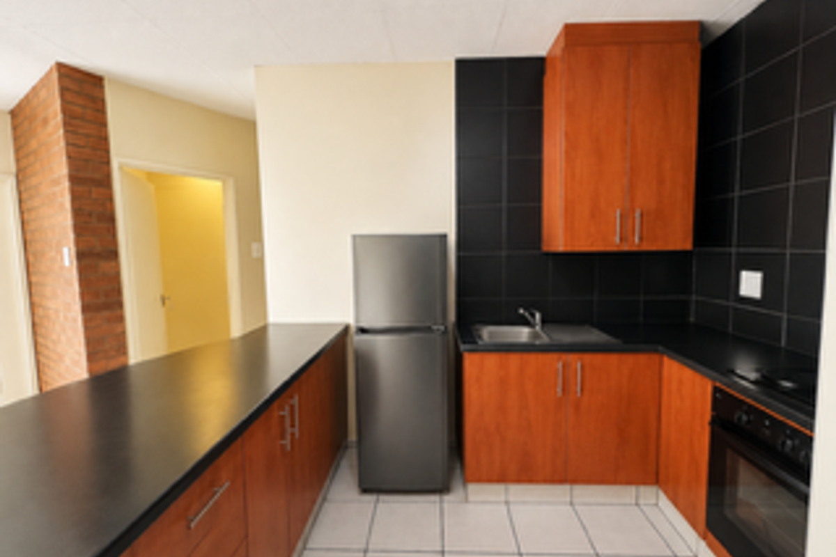 A functional kitchen featuring wood-finish cabinetry, black countertops, a built-in oven, and a contrasting black tiled backsplash.