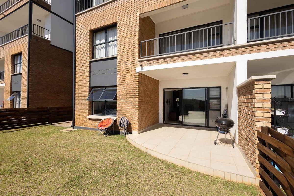 Rear view of the apartment featuring a paved patio area, brick facade, and a private lawn with timber fencing.