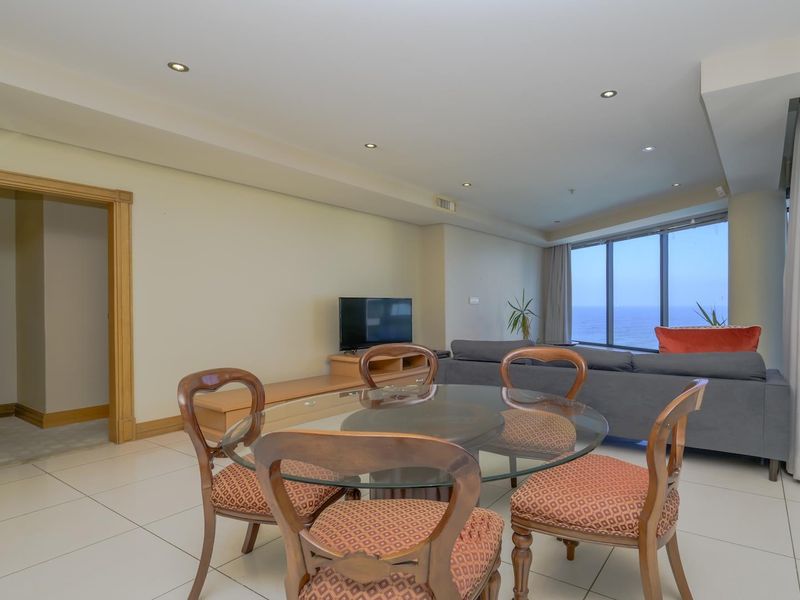 Spacious open-plan living and dining area featuring large windows with ocean views, neutral tiled flooring, and recessed lighting.