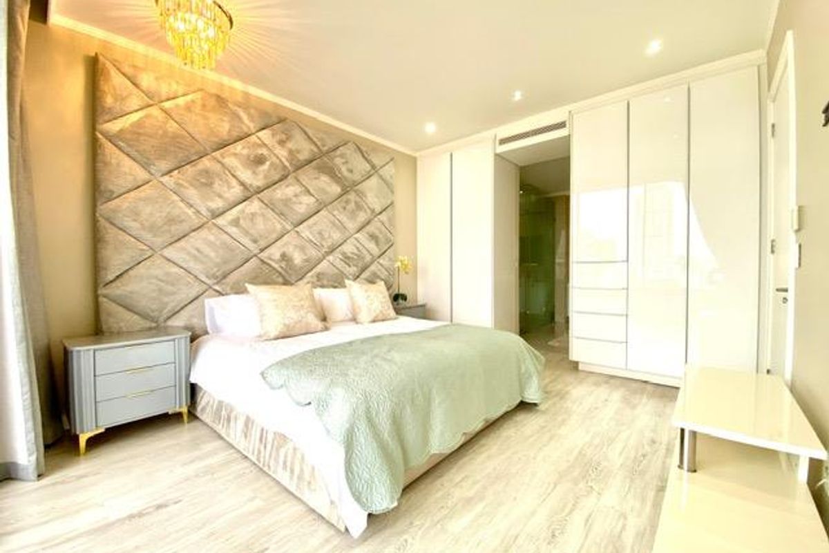 A well-appointed bedroom featuring a large upholstered headboard, integrated floor-to-ceiling cabinetry, recessed lighting, and light-toned wood-look flooring.