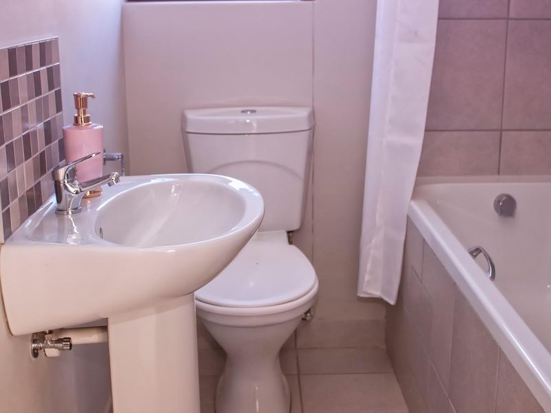 A functional bathroom featuring a pedestal basin, toilet, and bathtub with neutral wall and floor tiling.