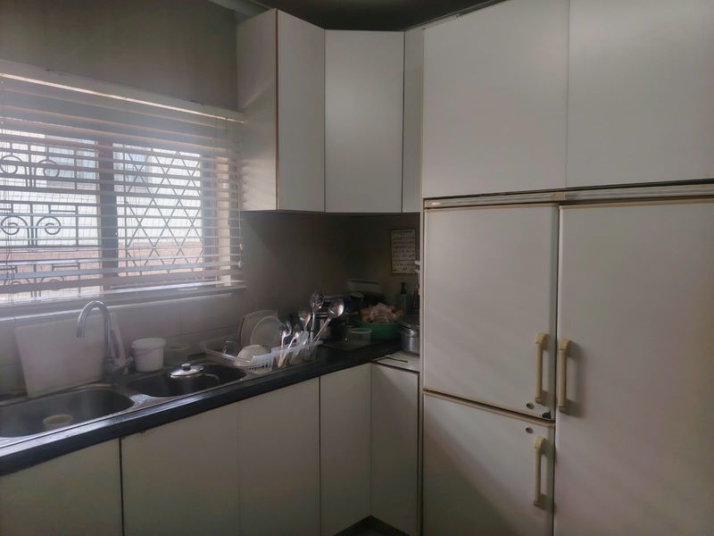 A functional kitchen featuring white built-in cabinetry, a double stainless steel sink with mixer tap, and laminate countertops, illuminated by natural light through a window.