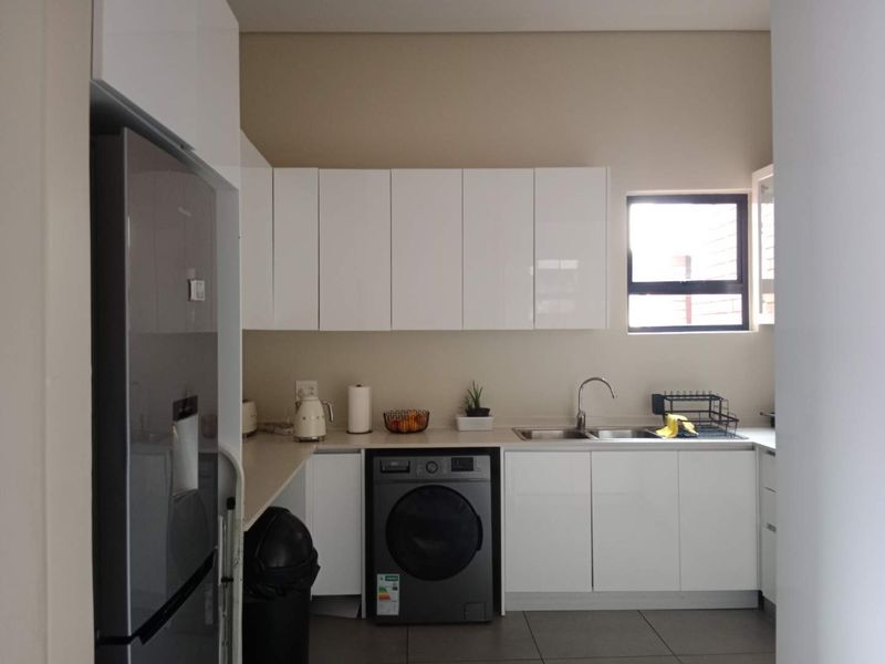 A modern kitchen featuring white gloss cabinetry, tiled flooring, a stainless steel sink, and a dedicated space for a washing machine.